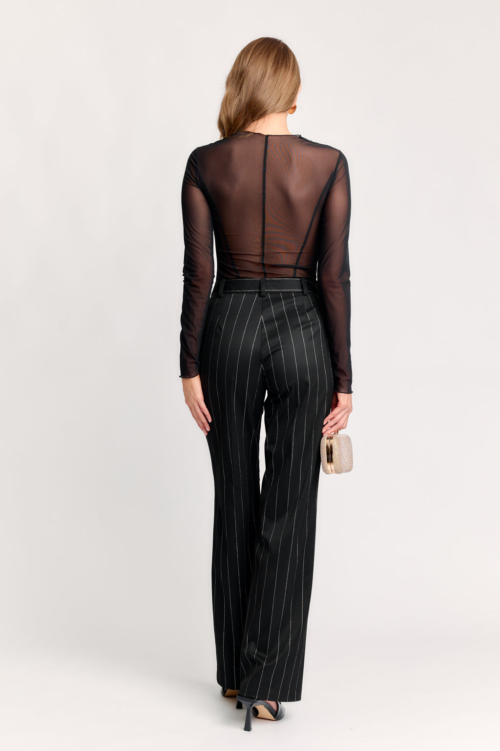 Woman wearing a sheer long-sleeve top and pinstripe pants on a white background