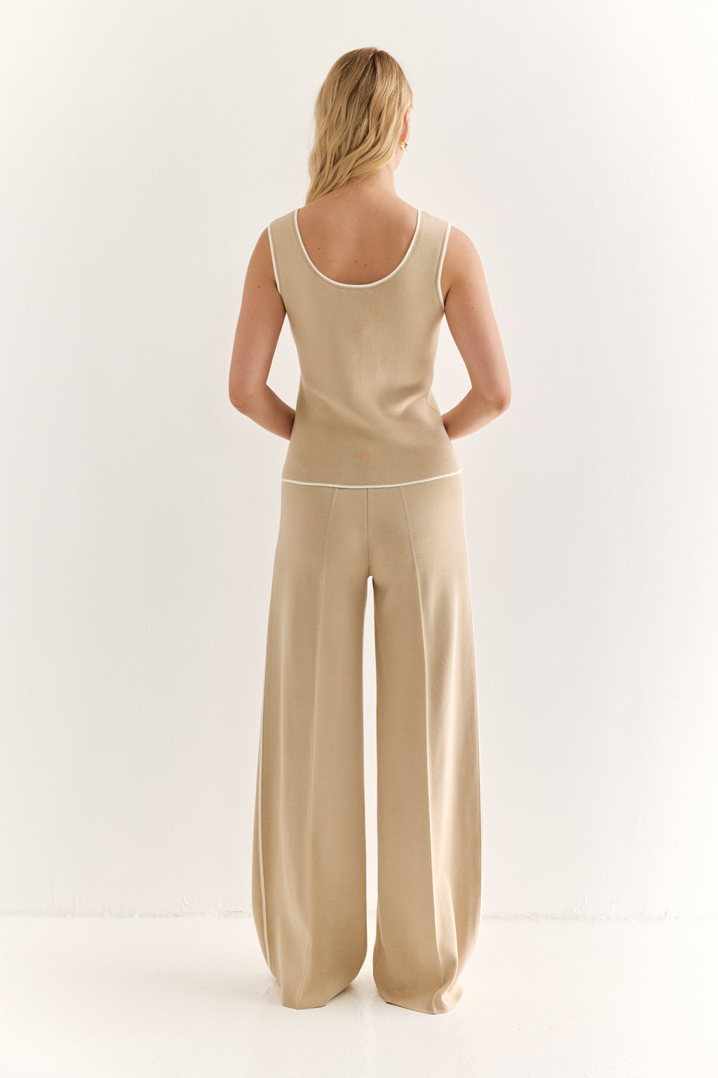 Woman wearing a beige sleeveless top and wide-leg pants on a white background