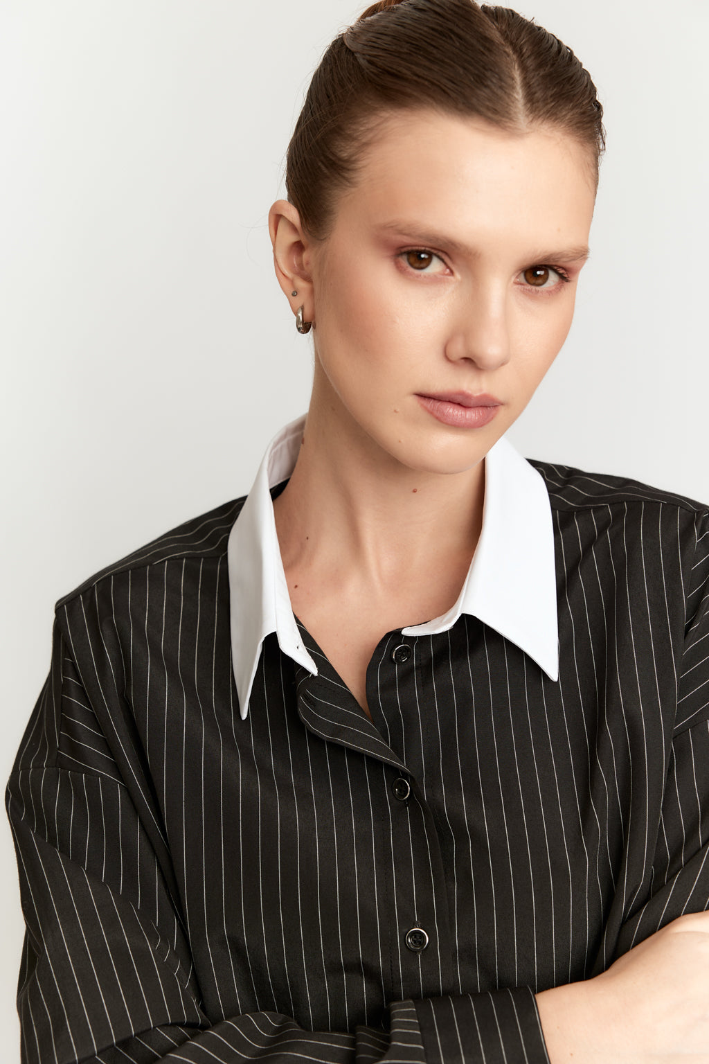 Woman wearing a black pinstripe shirt with a white collar against a plain background