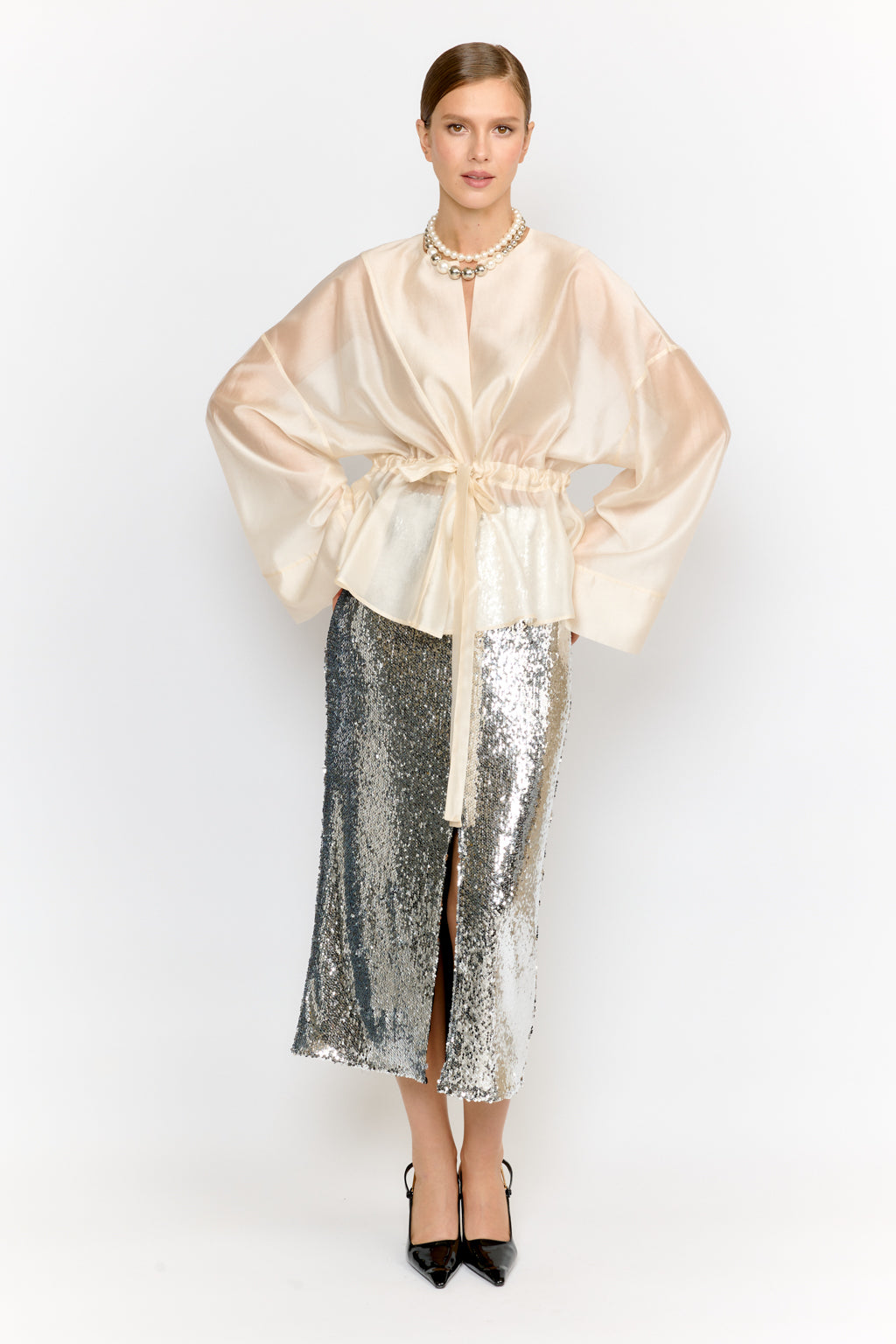 Woman wearing a beige satin robe over a silver sequin skirt on a white background