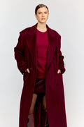 Person wearing a long burgundy coat over a matching dress on a white background