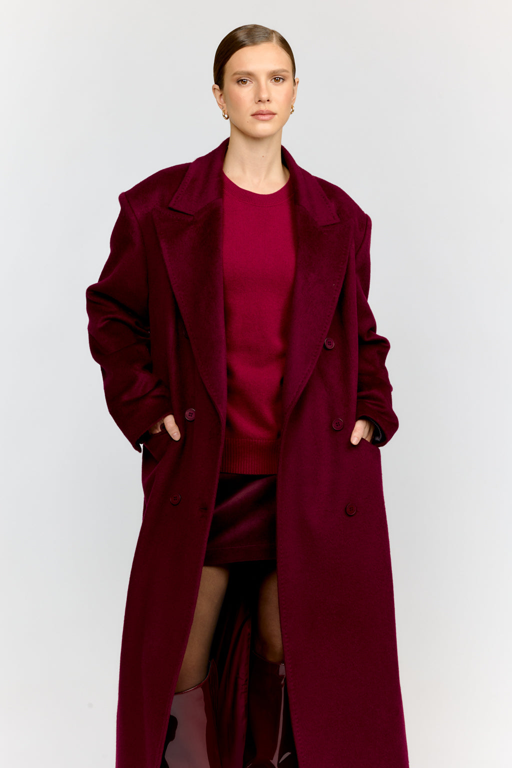 Person wearing a long burgundy coat over a matching dress on a white background