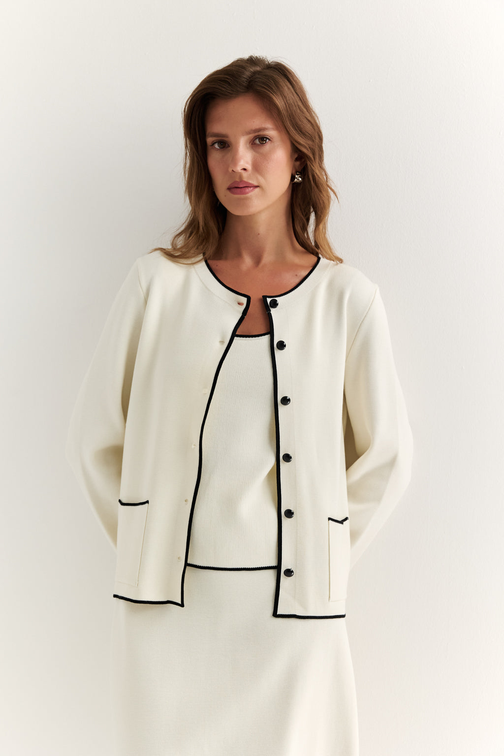 Woman wearing a white outfit with black trim on a plain background