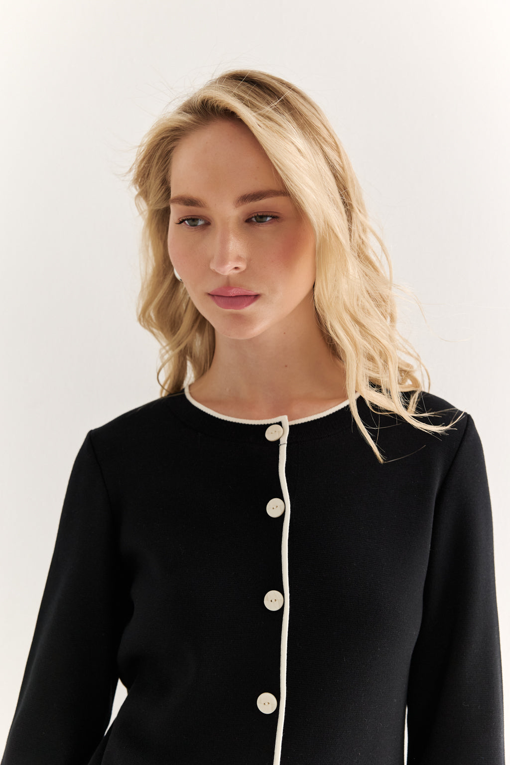 Woman wearing a black outfit with white buttons against a plain background