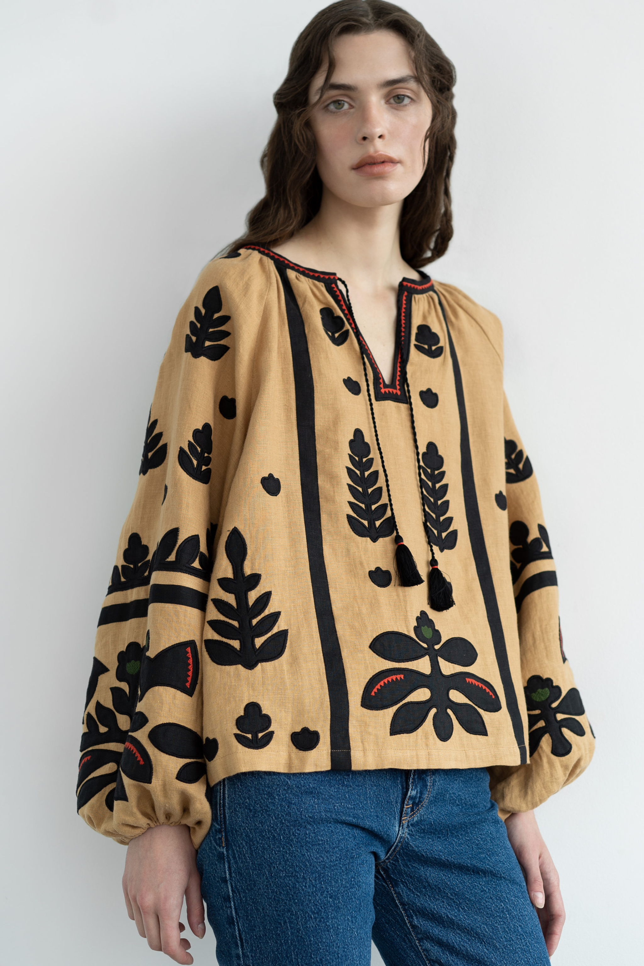Woman wearing a beige blouse with black floral patterns against a white background