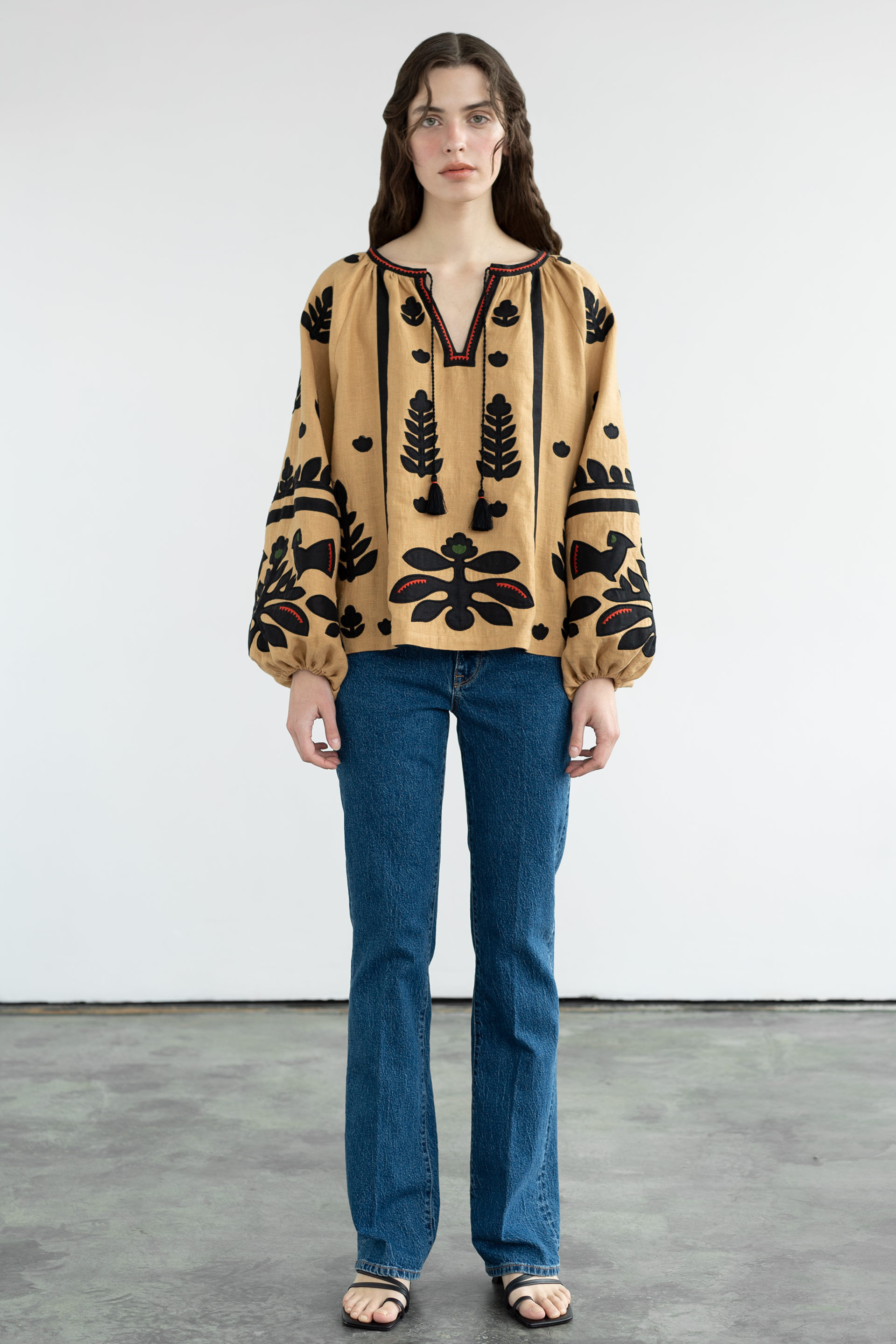 Woman wearing a patterned blouse and blue jeans against a white background
