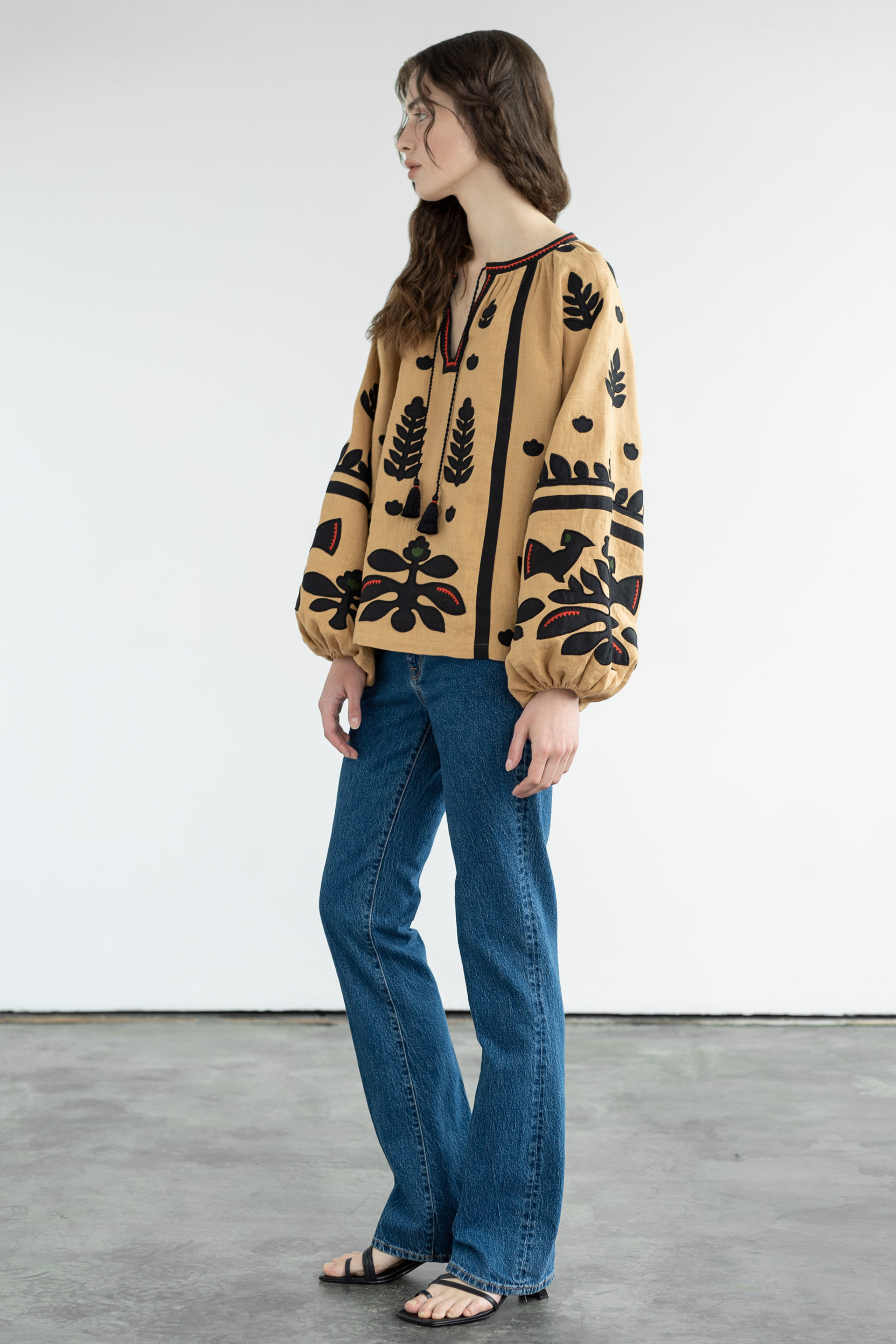 Woman wearing a patterned blouse and blue jeans against a white background