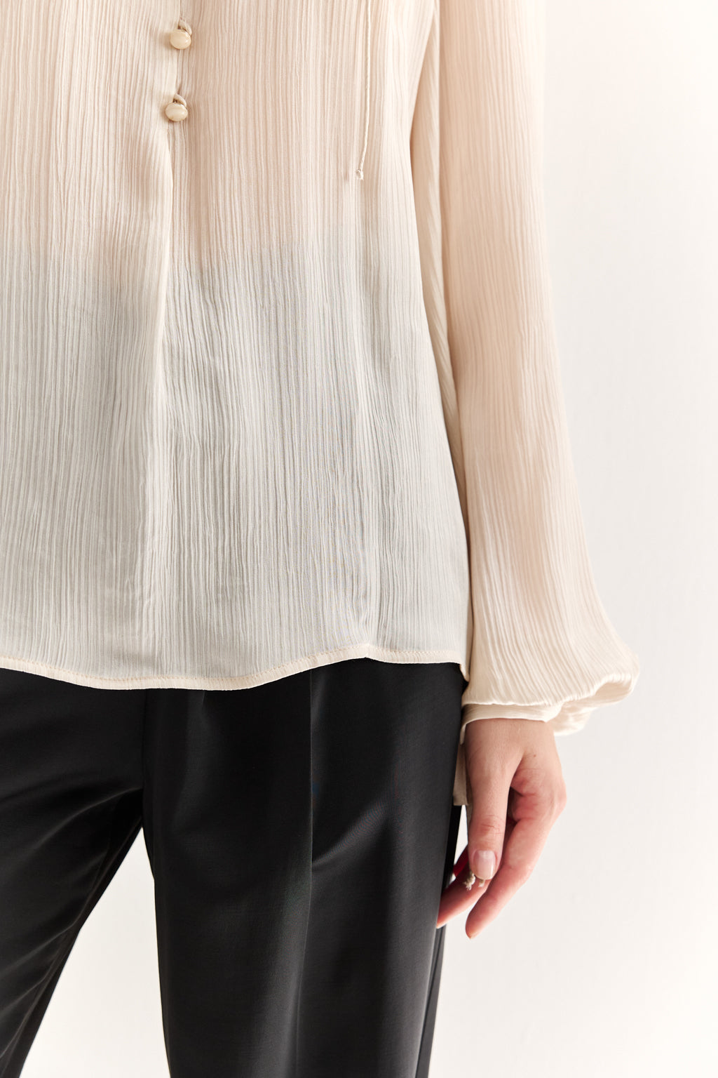Close-up of a person wearing a beige pleated blouse and black pants on a white background