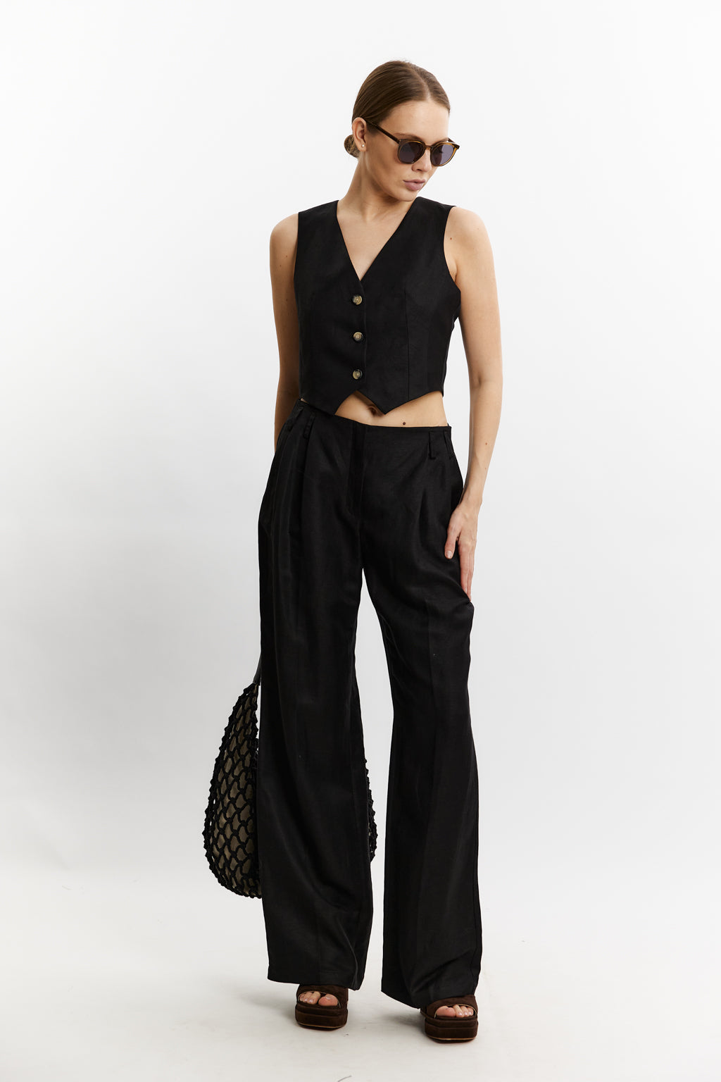 Woman wearing a black sleeveless top and wide-leg pants with sunglasses on a white background