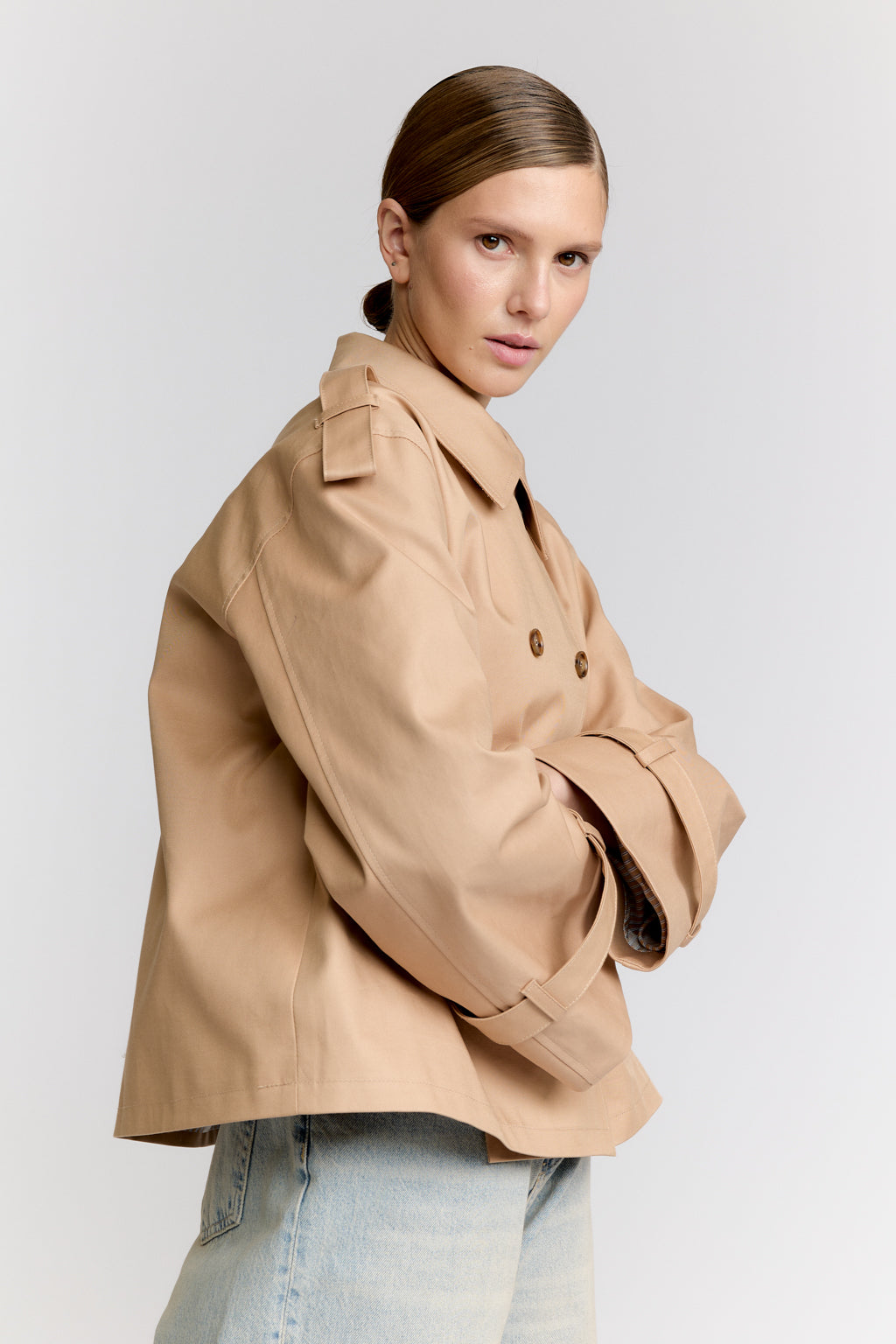 Woman wearing a beige trench coat on a plain background