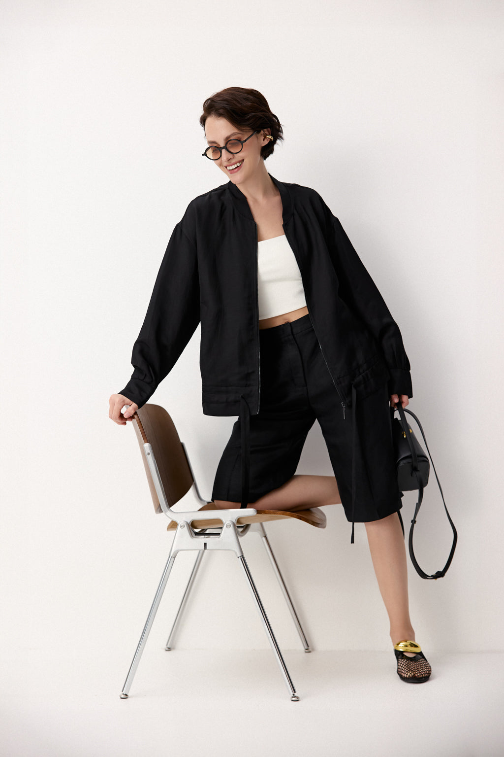 Woman in black outfit with white top sitting on a chair against a white background