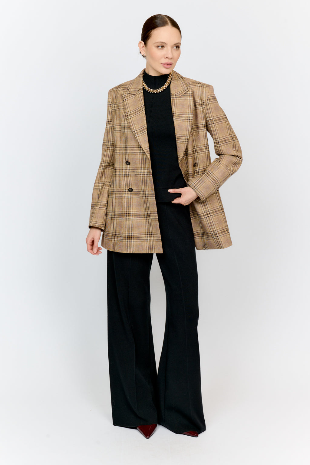 Woman wearing a beige checkered blazer and black pants on a white background