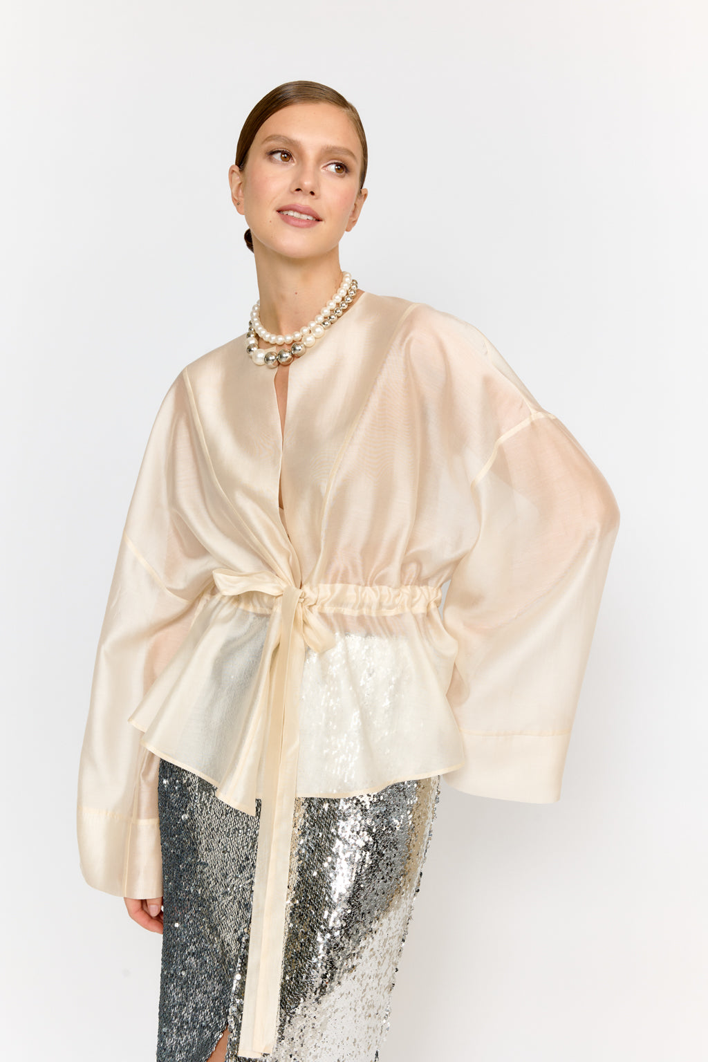 Woman wearing a beige satin robe over sequin pants on a white background