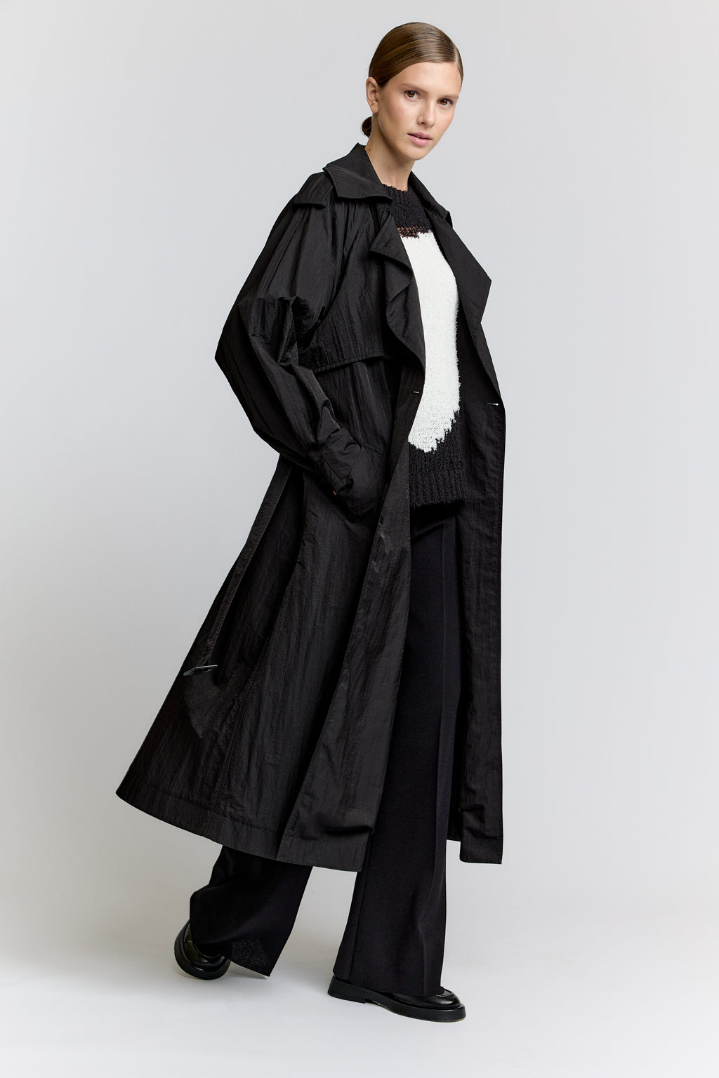 Person wearing a long black coat with a white shirt underneath on a light gray background