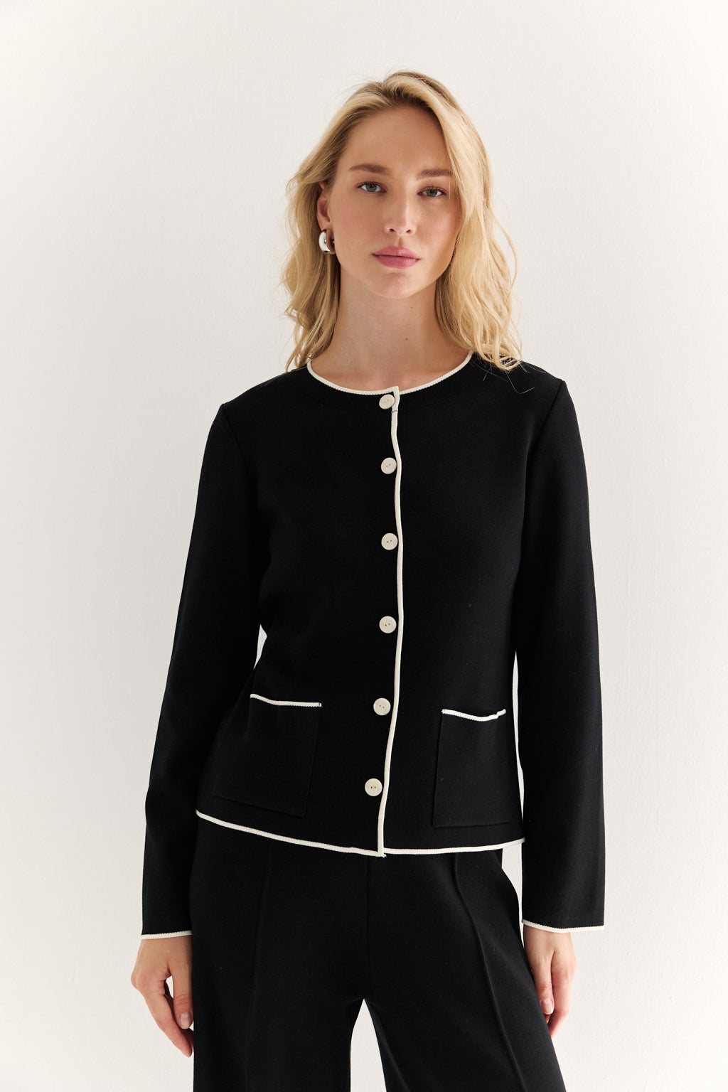 Woman wearing a black outfit with white buttons on a white background
