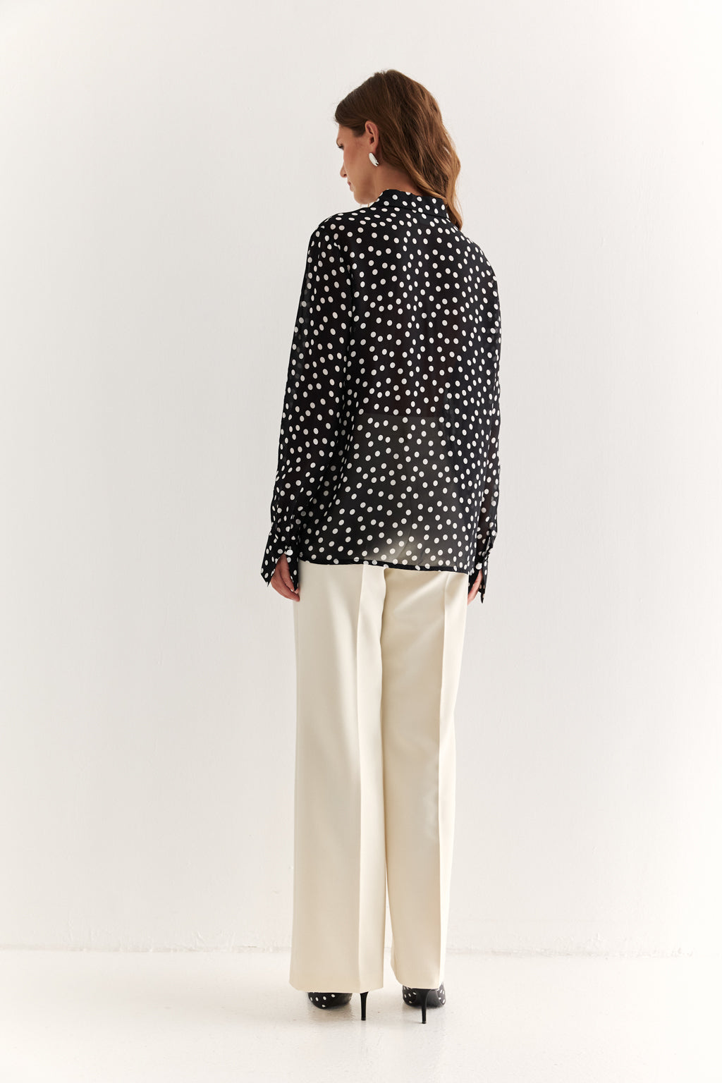 Woman wearing a black polka dot blouse and white pants on a white background