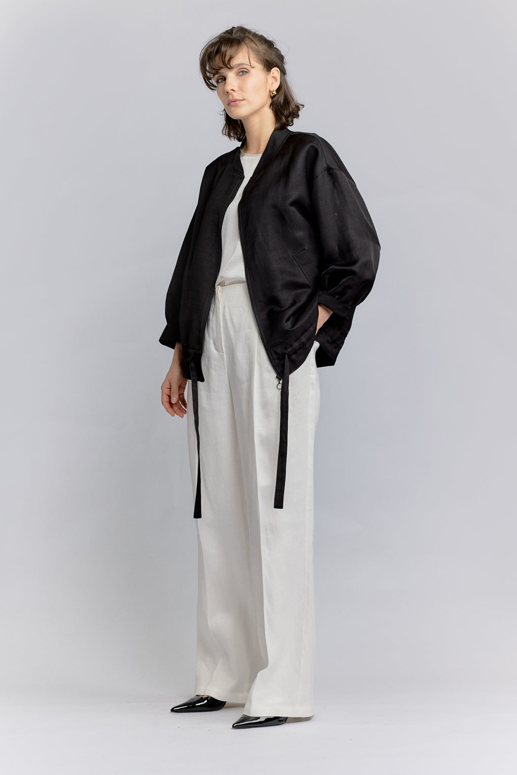 Person wearing a black jacket and white pants on a light gray background