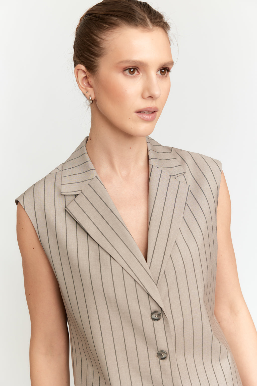 Woman wearing a beige pinstripe vest against a white background