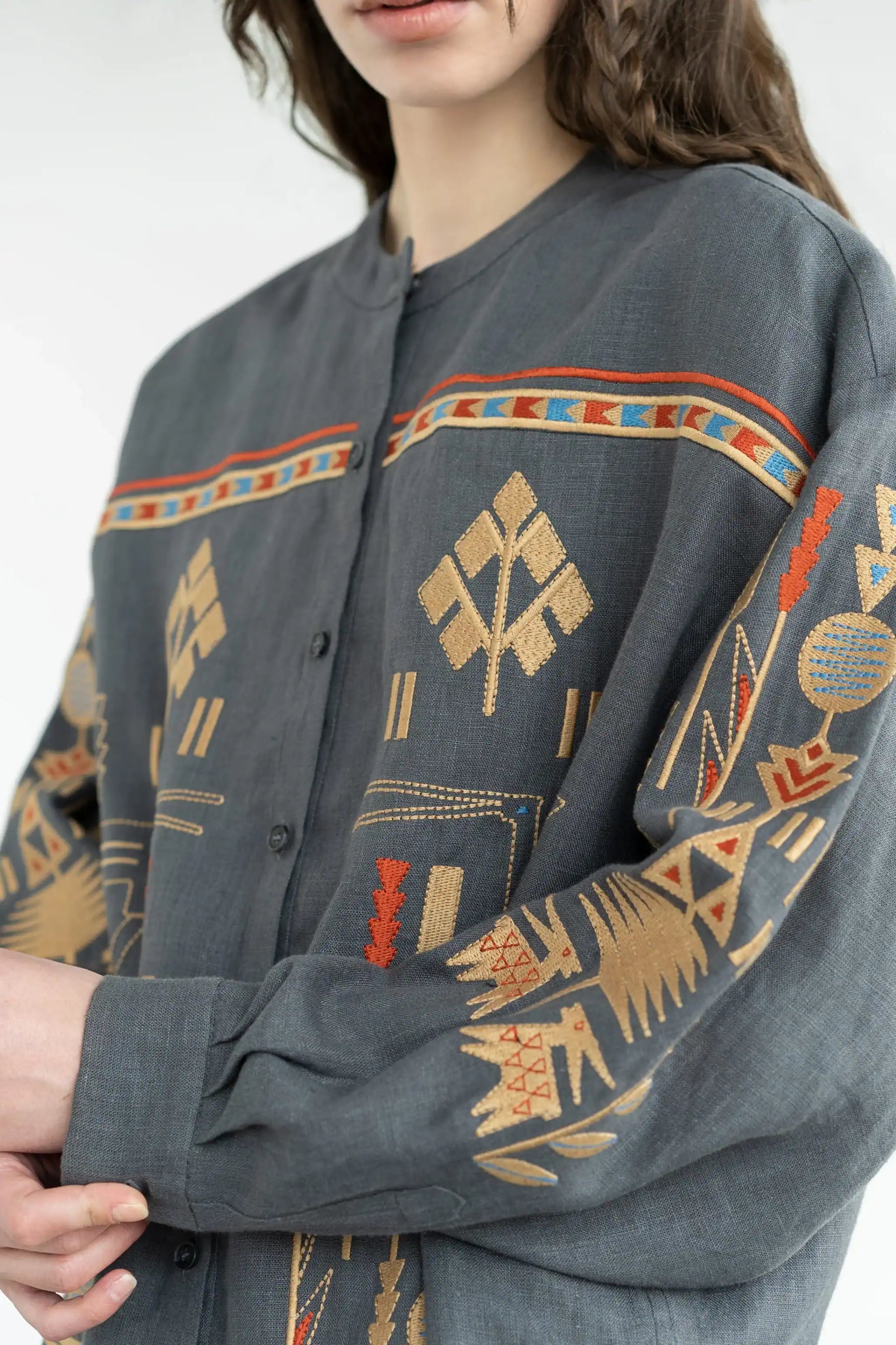 A close-up of a person wearing a dark gray button-front shirt with colorful geometric and tribal-inspired embroidery in beige, orange, and blue.