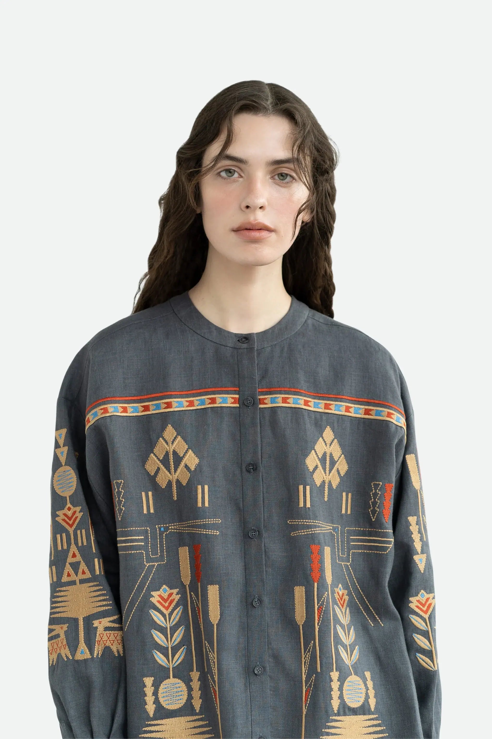 A model wearing a dark gray button-up shirt with a colorful geometric and botanical tribal pattern in beige, orange, and red, set against a plain light gray background.