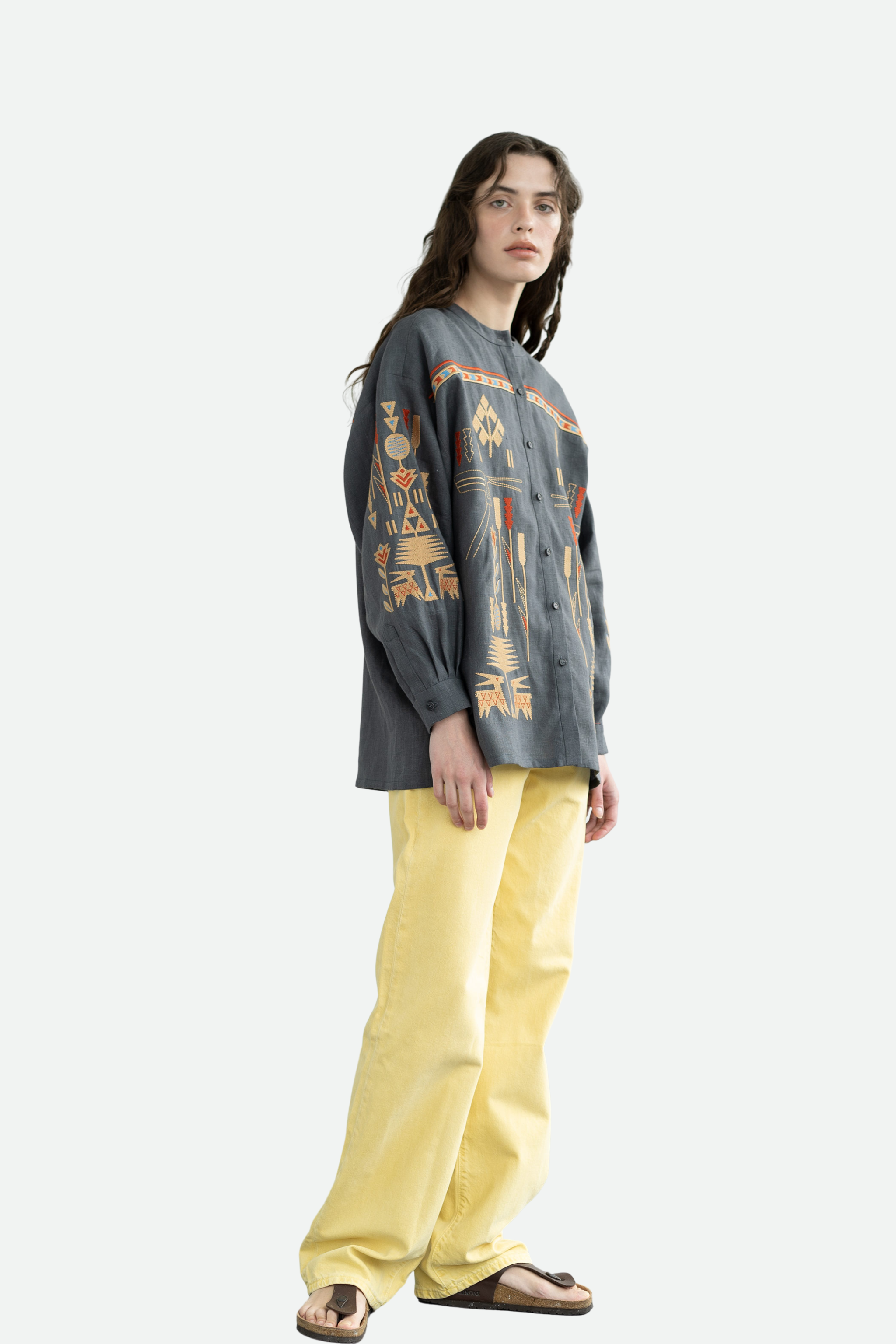 Person wearing a patterned long-sleeve shirt and yellow pants on a white background