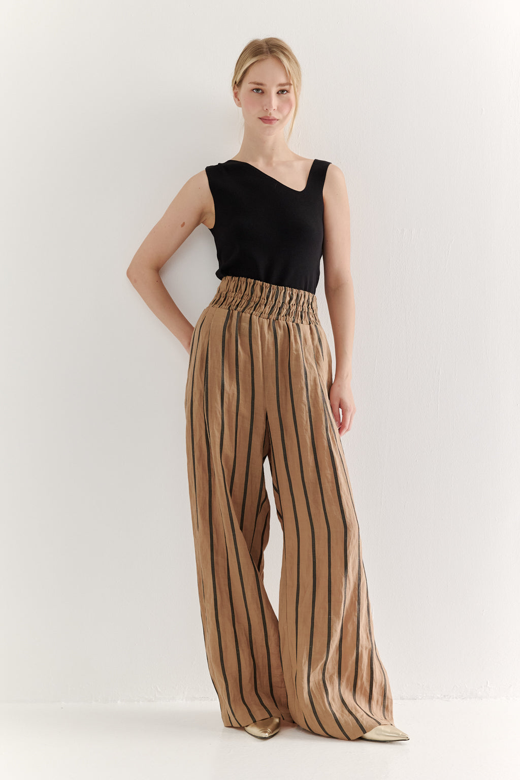 Woman wearing a black top and tan striped pants on a white background