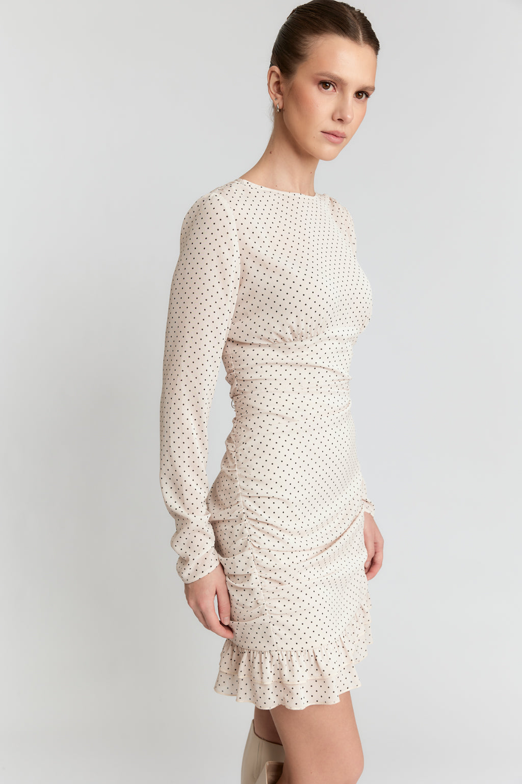 Woman wearing a white dress with long sleeves and ruffled hem on a light gray background