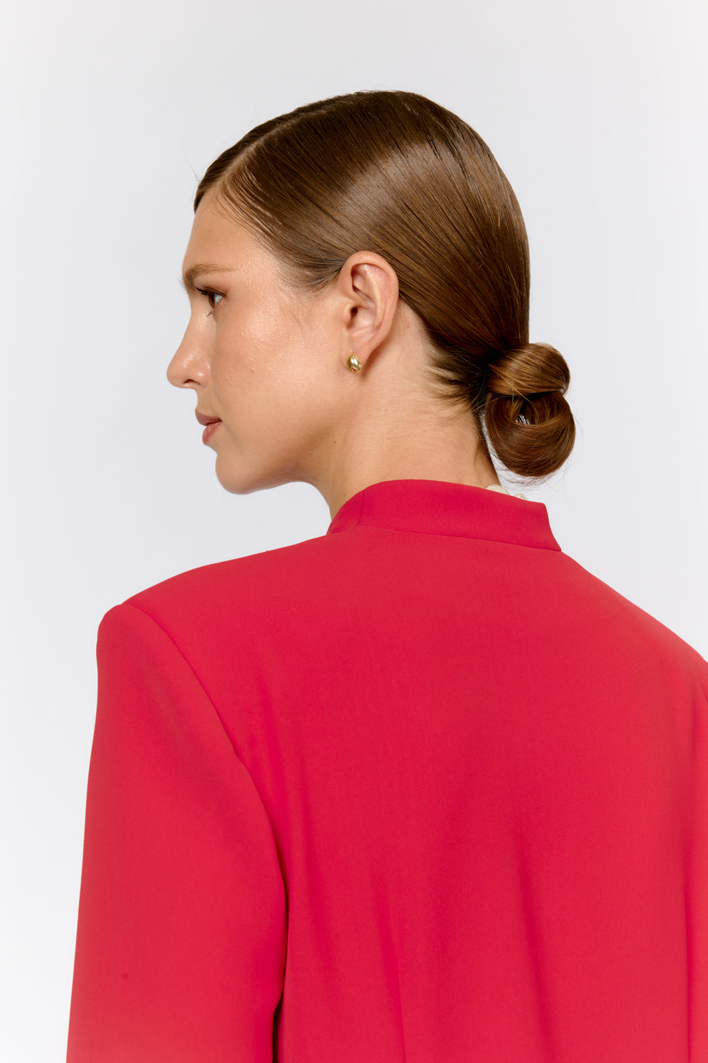 Woman in a red jacket with her hair styled in an updo against a white background