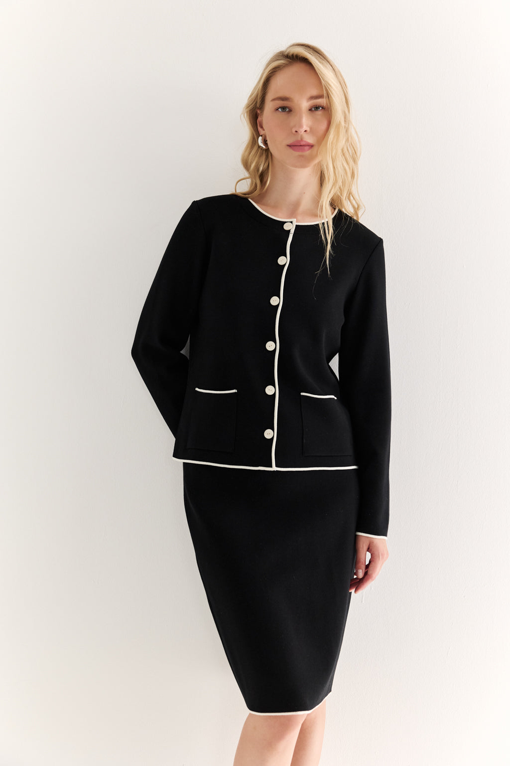 Woman wearing a black suit with white buttons against a white background