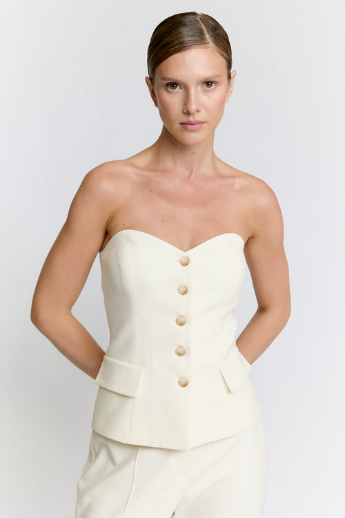 Woman wearing a strapless cream top with button details on a plain background