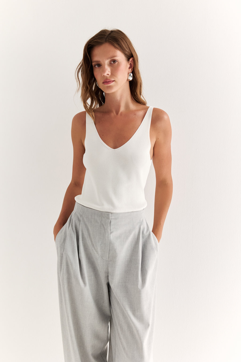 Woman wearing a white tank top and gray pants against a plain background