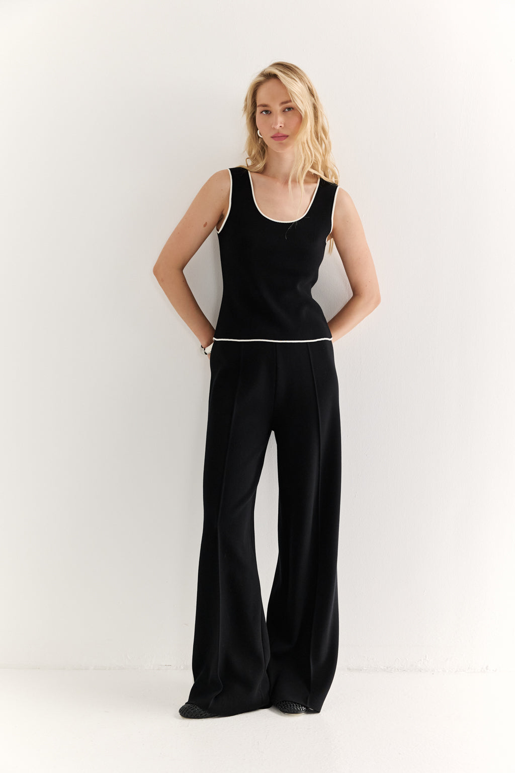 Woman wearing a black sleeveless top and wide-leg pants on a white background