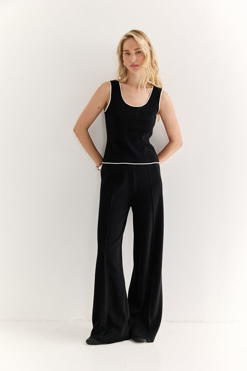 Woman wearing a black sleeveless top and wide-leg pants on a white background