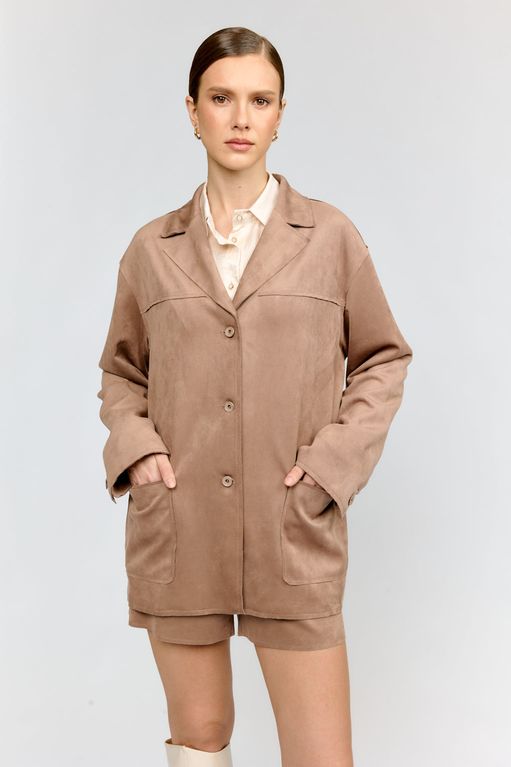 Woman wearing a beige coat and shorts on a plain background