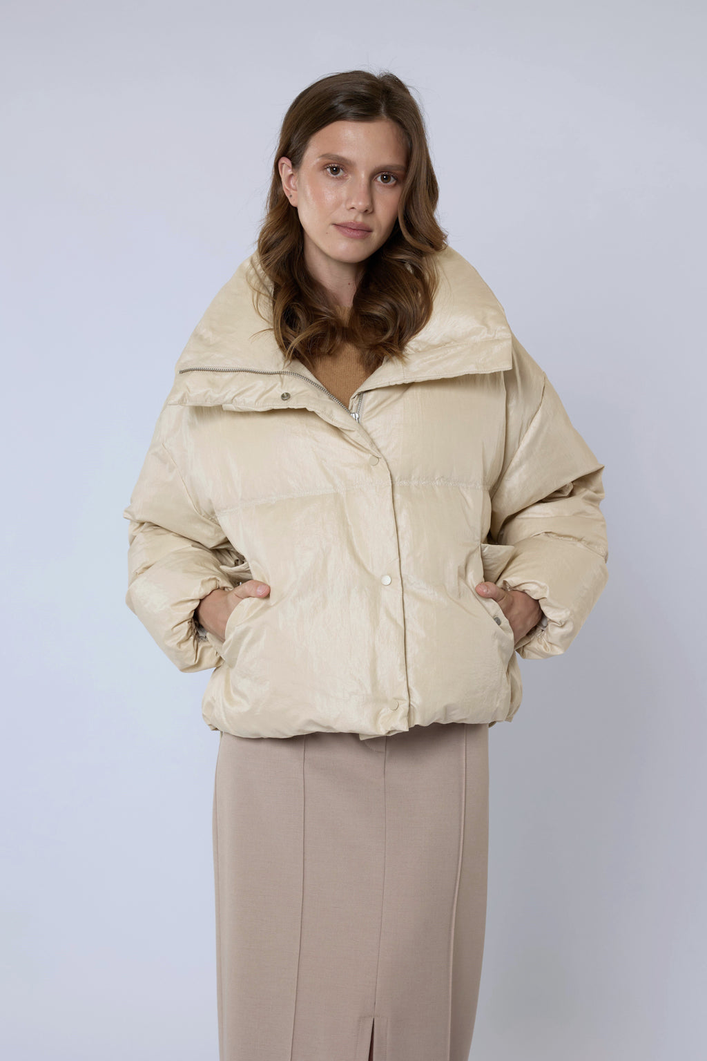 Woman wearing a beige puffer jacket against a light purple background