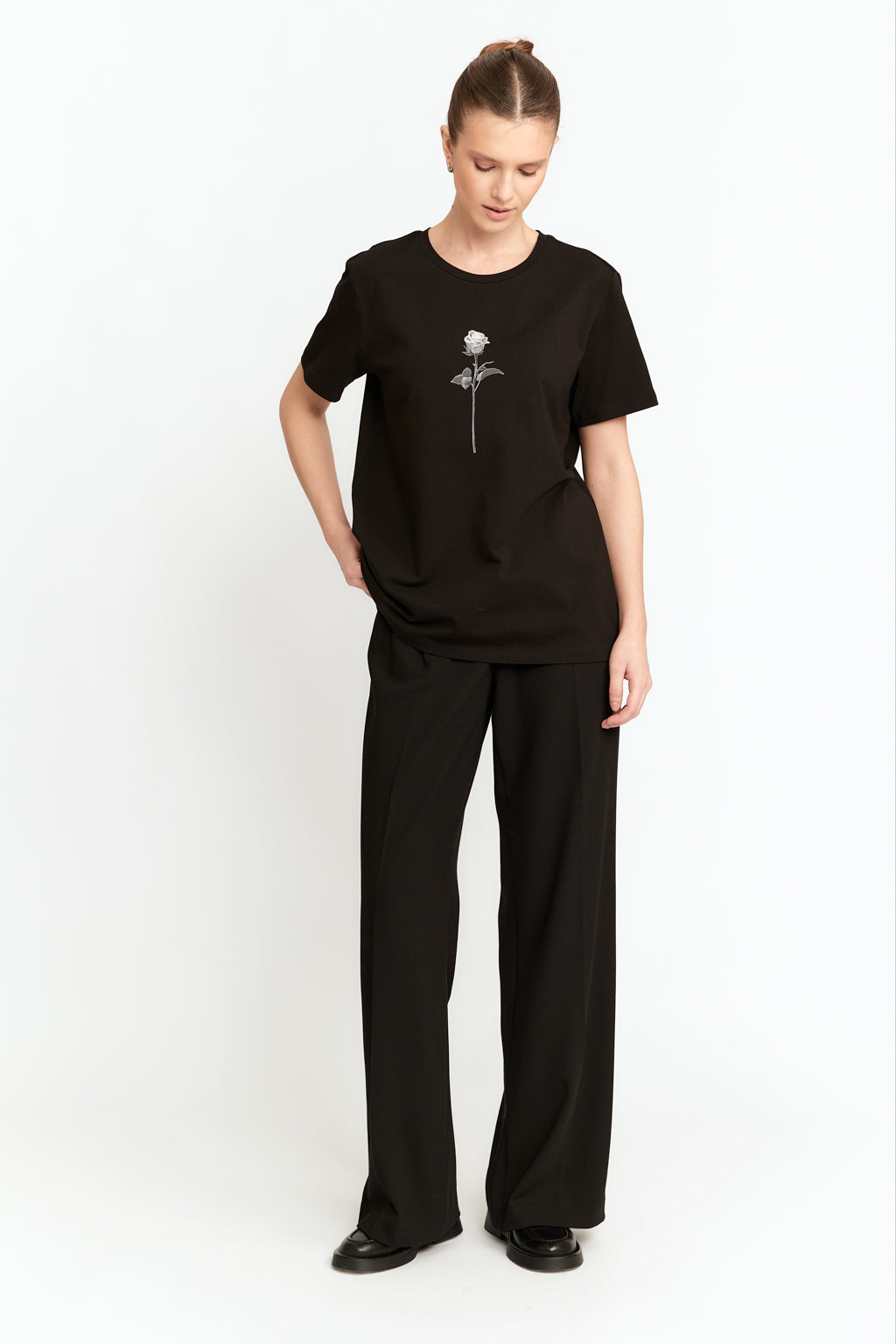 Person wearing a black t-shirt with a flower design and black pants on a white background