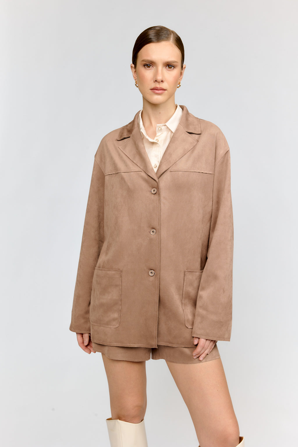 Woman wearing a brown coat and shorts on a light gray background