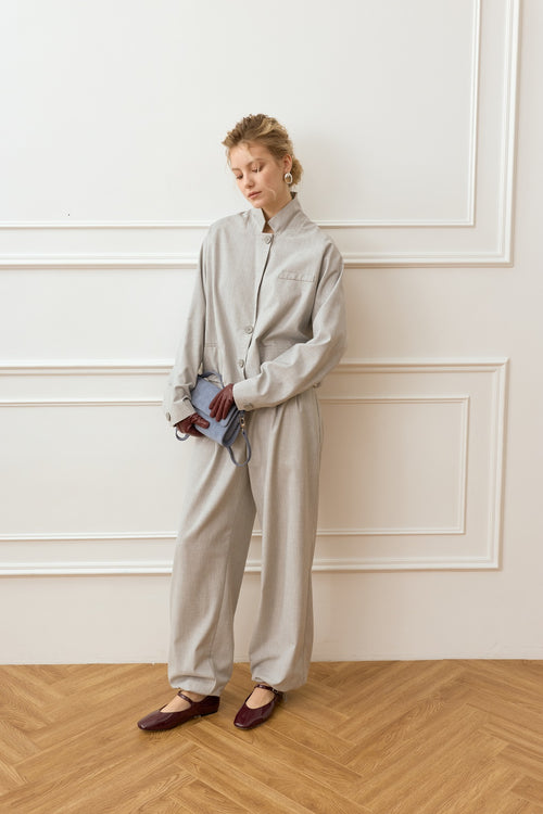 Woman in a light gray outfit standing against a white paneled wall.