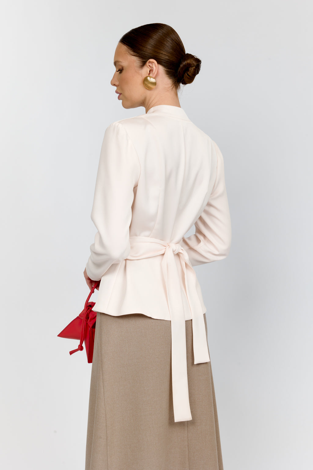 Woman wearing a white blouse with a red ribbon and beige skirt on a light gray background