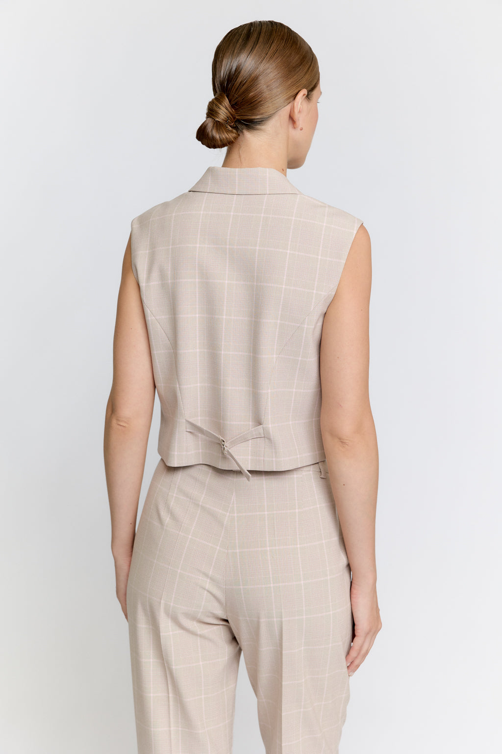 Woman wearing a beige checkered vest and pants on a white background