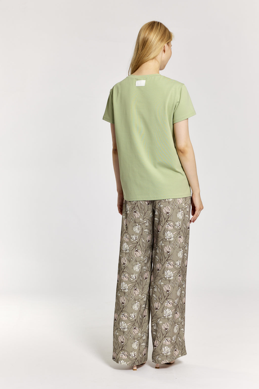 Woman wearing a light green t-shirt and patterned pants on a white background
