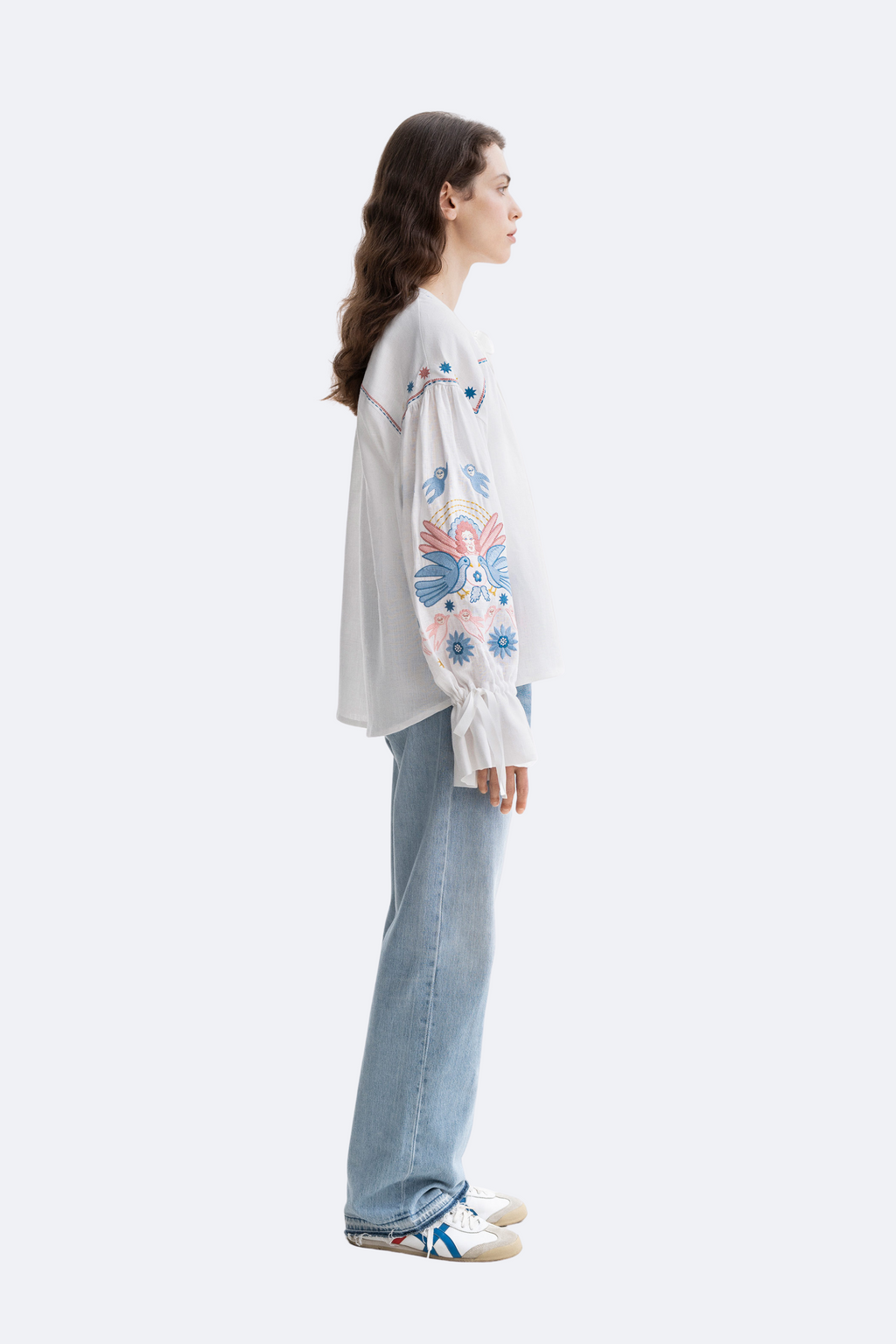 Person wearing a light gray sweatshirt with floral patterns and blue jeans on a white background