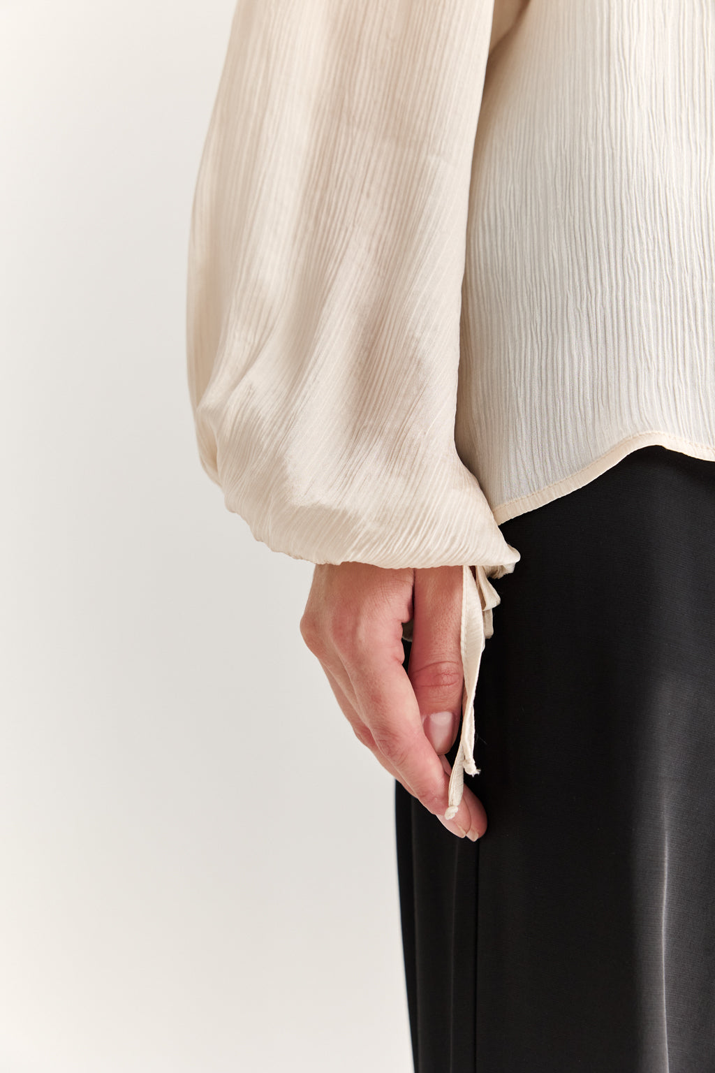Close-up of a person wearing a beige blouse with puffed sleeves and black pants on a white background