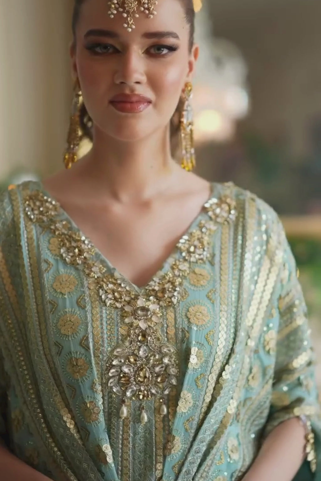 Woman wearing an ornate, light green dress with gold embroidery and jewelry.