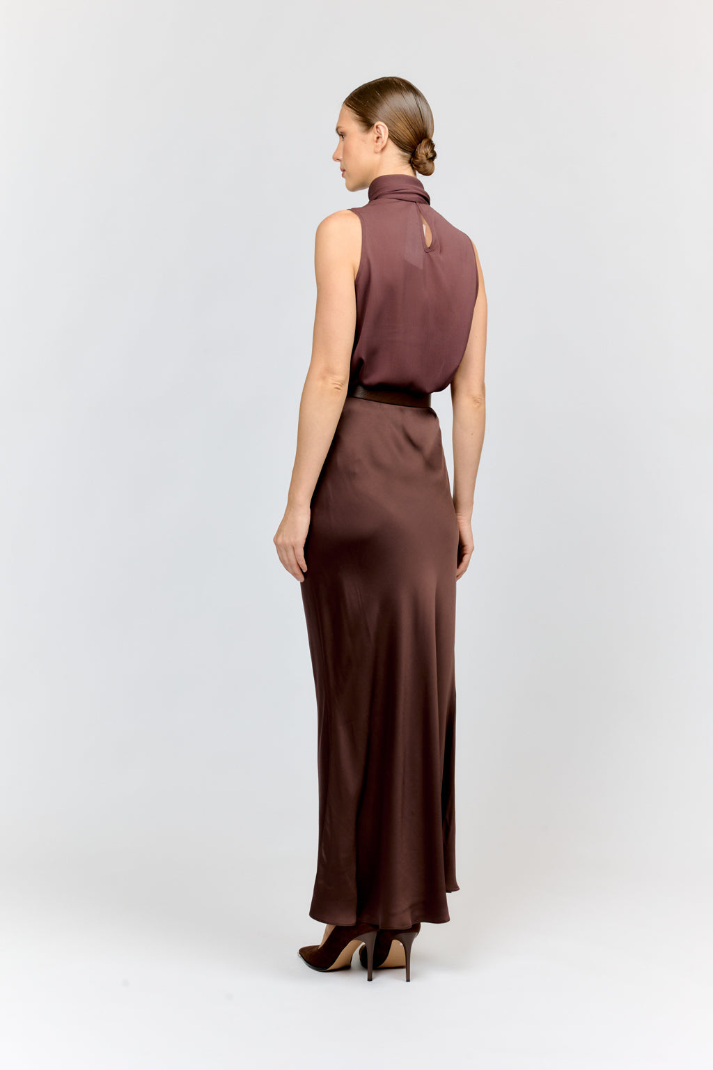 Woman wearing a sleeveless burgundy top and long skirt on a white background