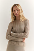 Woman wearing a beige cable knit sweater against a white background