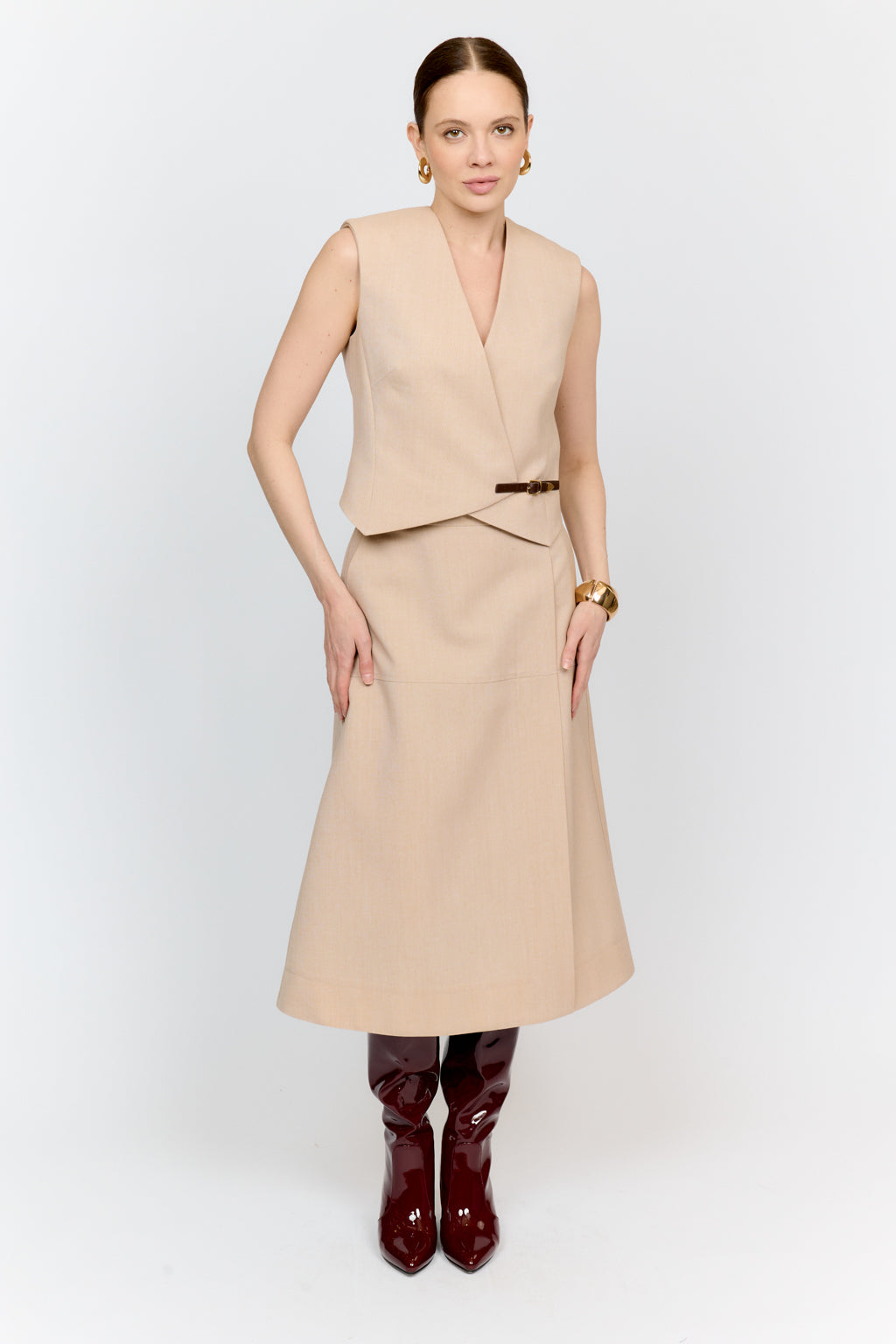 Woman wearing a beige dress with a vest and brown boots on a white background