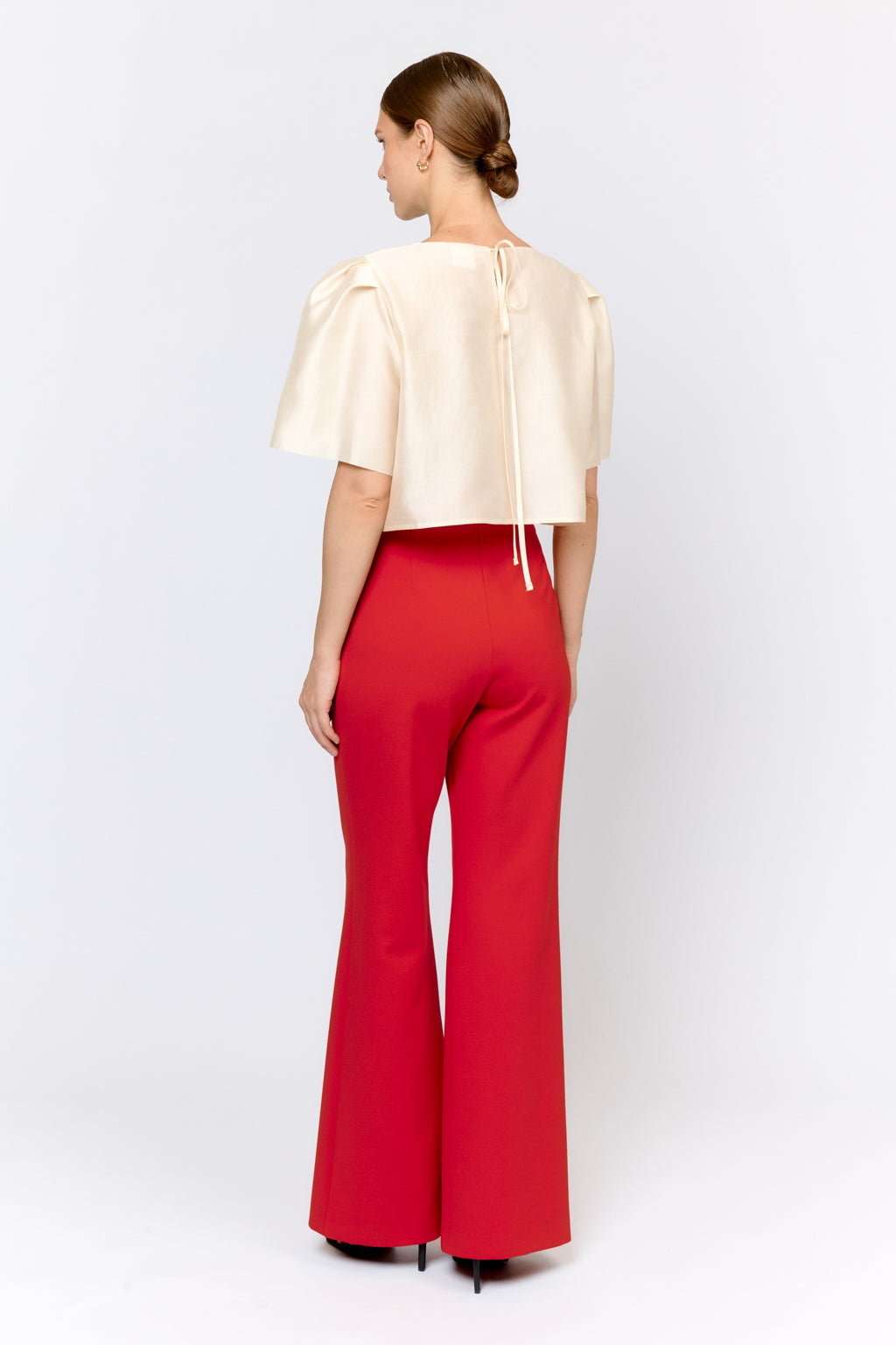 Woman wearing a cream top and red pants on a white background