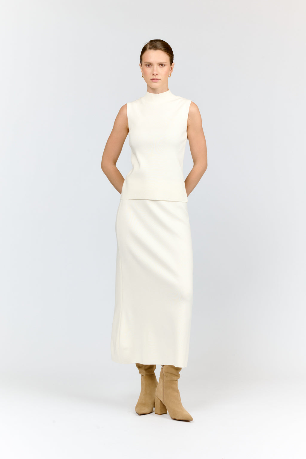 Woman wearing a white dress with beige boots on a light gray background