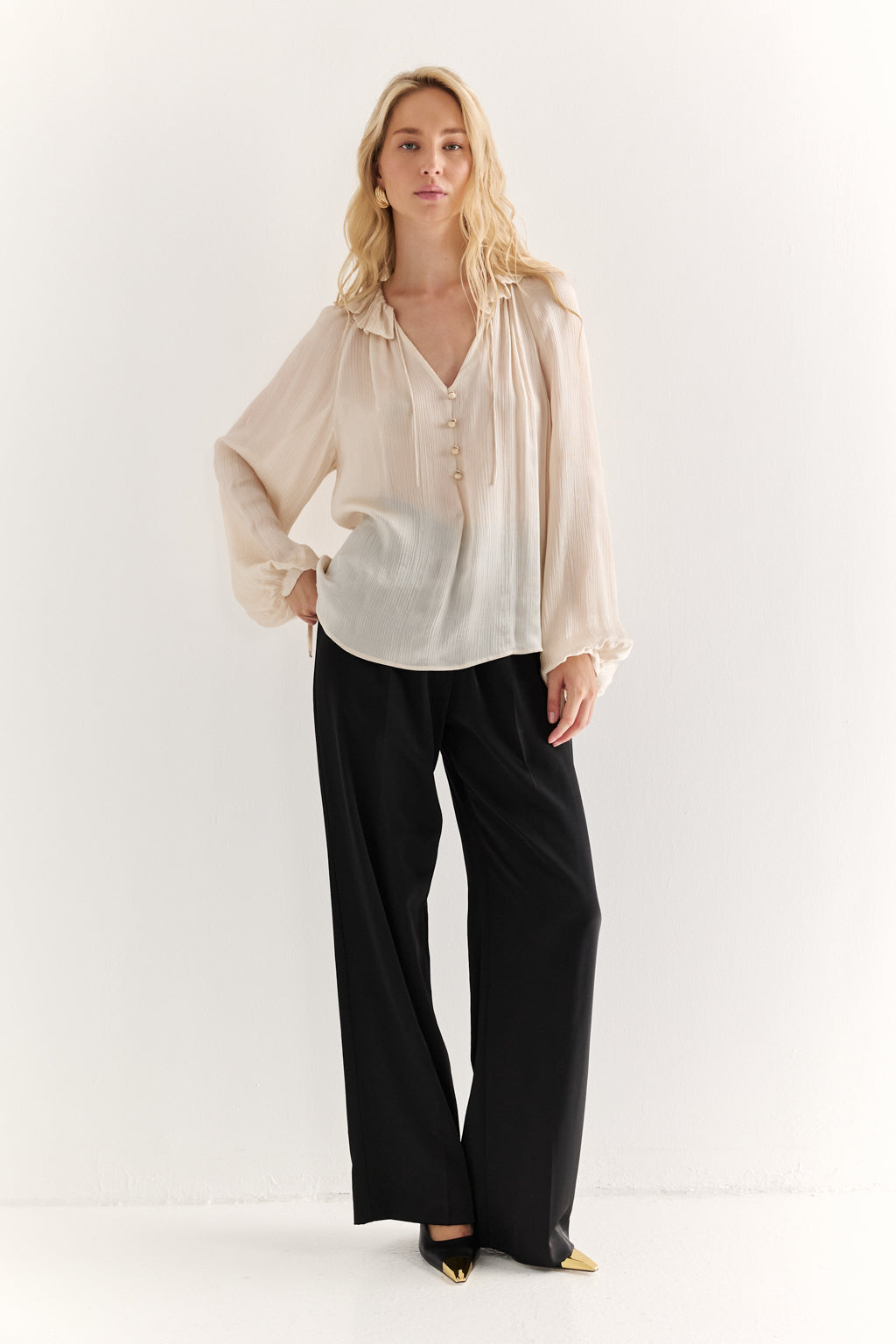 Woman wearing a beige blouse and black pants on a white background